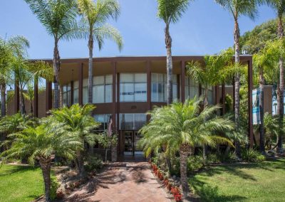 Rio Honda Subacute and Nursing Center 2 story from entrance flanked by palm trees.